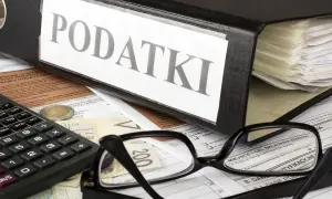 Segregator z napisem "PODATKI", kalkulator, okulary i dokumenty. Obok leży moneta, symbolizująca potencjalną kwotę zmniejszającą podatek.