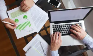 Dwóch mężczyzn analizuje wykresy i dane na laptopie. Dyskusja dotyczy prawdopodobnie efektywności podatku progresywnego.