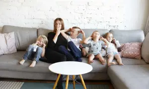 Mama z gromadką dzieci, cała rodzina wielodzietna, siedzą na kanapie i robią śmieszne miny.
