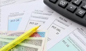 Formularze PIT, polskie banknoty, żółty długopis i kalkulator.