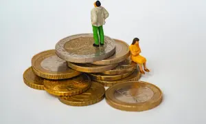 Figurki ludzi na stosie monet. Jedna osoba stoi na szczycie, druga siedzi obok. Symbolizuje to opłatę skarbową i jej wpływ na finanse.