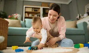 Mama bawi się z dzieckiem na dywanie, budując tory dla pociągu. To czas na zabawę i rozwijanie umiejętności, czyli aktywnie w pracy nad rozwojem malucha.