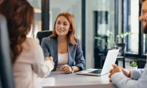 Uśmiechnięta kobieta podaje rękę, omawiając kredyt na dowód bez umowy o pracę.