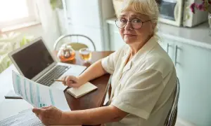 Kobieta z okularami analizuje dokumenty, planując emeryturę za 4 dzieci. Na stole laptop, herbata i notatnik.