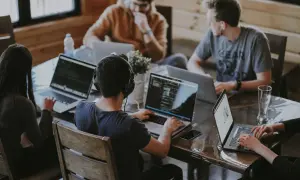 Grupa osób pracuje przy laptopach, dyskutując o regulaminie pracy.