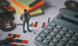 Figurka mężczyzny, kalkulator, monety i wykresy. Czy to syndyk, kto to? Analiza finansowa.