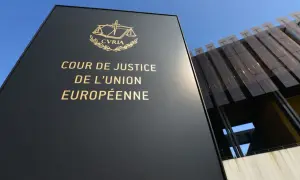 Czarny szyld z napisem "COUR DE JUSTICE DE L'UNION EUROPÉENNE" i symbolem wagi. W tle nowoczesny budynek.
