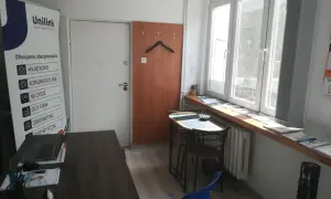 Biuro Unilink z banerem informacyjnym, biurkiem z laptopem i oknem.