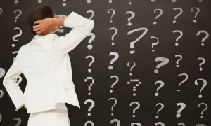 Kobieta w białym garniturze drapie się po głowie na tle tablicy z licznymi znakami zapytania. Czy to decyzja o wydziedziczeniu?
