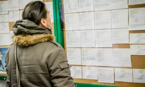 Mężczyzna w zimowej kurtce analizuje ogłoszenia na tablicy, szukając informacji o umowie zlecenie i składkach.