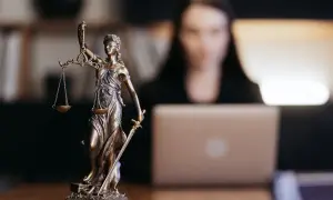 Figurka Temidy symbolizuje sprawiedliwość w sprawach o wydziedziczenie a zachowek. Kobieta pracuje przy laptopie.