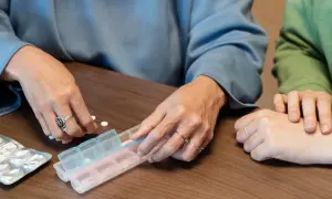 Dwie osoby sortują tabletki w pojemniku na leki. Dostępne są darmowe leki dla seniorów.