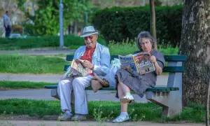 Starsza para, jak spółka partnerska, czyta gazety na ławce w parku.