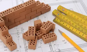 Miniaturowa budowa na planie architektonicznym: cegły, miarka i ołówek. To jakby planistyczna zabawa w budowanie.