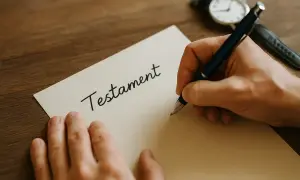 Ręka pisze długopisem słowo "Testament" na kartce. Obok leży zegarek.