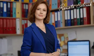 Kobieta w niebieskiej marynarce stoi przed regałami z kolorowymi segregatorami.