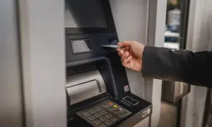 Dłoń wsuwa kartę do bankomatu, by sprawdzić, ile można wypłacić.