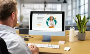 Mężczyzna pracuje przy komputerze, na ekranie którego widoczna jest strona internetowa agencji ubezpieczeniowej.