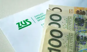 ZUS i polskie banknoty 100 zł. Pieniądze leżą obok koperty z logo ZUS, symbolizując finanse i ubezpieczenia społeczne.