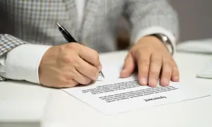 Mężczyzna w eleganckim garniturze podpisuje umowę przedwstępną sprzedaży nieruchomości.