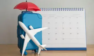 Błękitna walizka z parasolką i samolotem na tle kalendarza. Planujesz dodatkowy urlop?