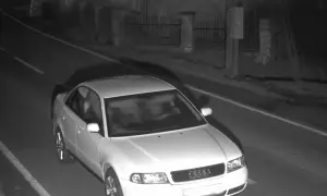 Biały sedan Audi jedzie nocą po drodze, prawdopodobnie zarejestrowany przez fotoradar.