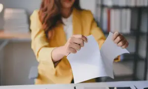 Kobieta w żółtej marynarce rozdziera dokument. Może to symbolizować wypowiedzenie za porozumieniem stron, kończące pewien etap.