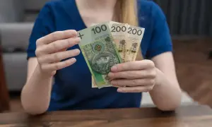 Ręce trzymają banknoty 100 i 200 zł. To wsparcie, które może pomóc w pokryciu kosztów związanych z opieką nad dzieckiem, jak zasiłek rodzicielski.