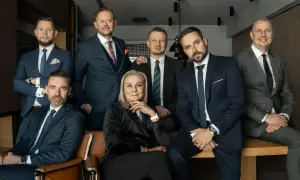 Grupa siedmiu profesjonalistów w garniturach, w tym jedna kobieta, pozuje do zdjęcia.
