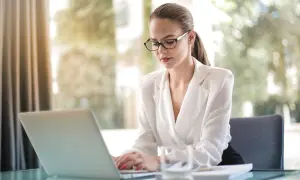 Kobieta w okularach pracuje na laptopie, planując swoją nierejestrowaną działalność gospodarczą.