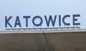 Napis "KATOWICE" z niebieskimi neonami na tle jasnego nieba, nad betonową konstrukcją.