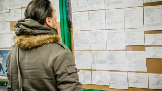 Mężczyzna w zimowej kurtce analizuje ogłoszenia na tablicy, szukając informacji o umowie zlecenie i składkach.