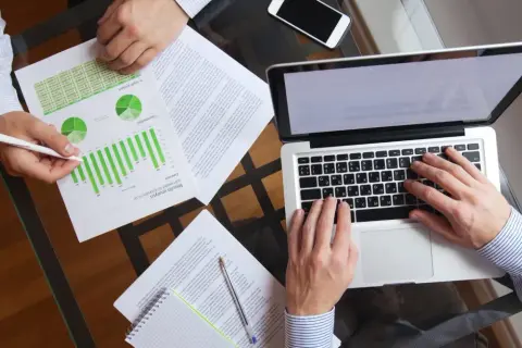 Dwóch mężczyzn analizuje wykresy i dane na laptopie. Dyskusja dotyczy prawdopodobnie efektywności podatku progresywnego.