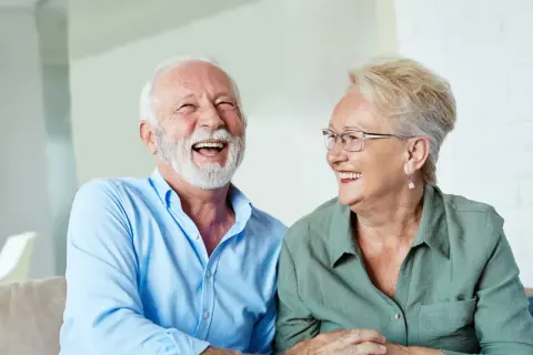 Szczęśliwi seniorzy śmieją się, omawiając zwrot podatku od 13 i 14 emerytury w tabeli.