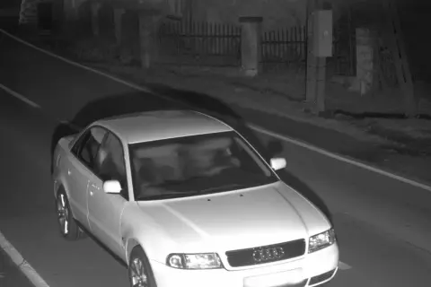 Biały sedan Audi jedzie nocą po drodze, prawdopodobnie zarejestrowany przez fotoradar.