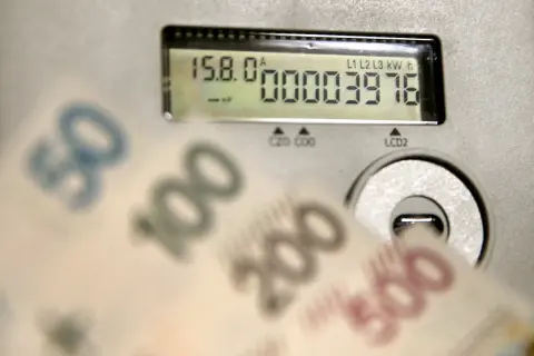 Licznik energii pokazuje zużycie 3976 kWh. W tle rozmazane banknoty 50, 100, 200, 500 zł, sugerujące wysoką cenę za kWh.