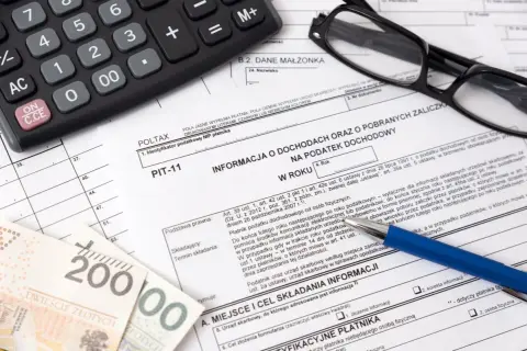 Na PIT-11 widoczne są dokumenty, kalkulator i pieniądze. Kwota zwrotu PIT-11 jest ukryta.