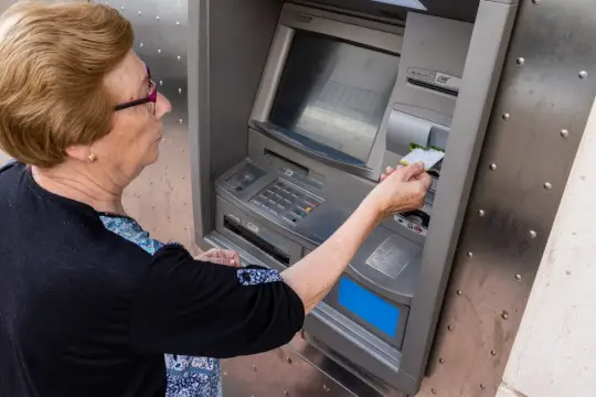 Starsza pani z kartą przy bankomacie. Może to jej dodatek do emerytury po 70 roku życia?
