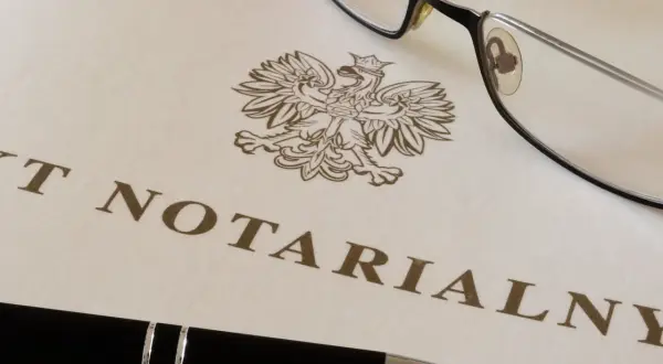 Okulary i długopis leżą na dokumencie z godłem Polski i napisem "AKT NOTARIALNY". To dokument, który wymaga opłaty, czyli taksa notarialna.