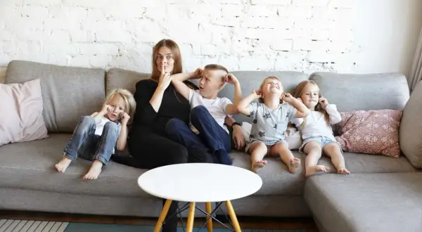 Mama z gromadką dzieci, cała rodzina wielodzietna, siedzą na kanapie i robią śmieszne miny.