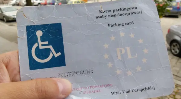 Karta parkingowa dla niepełnosprawnych, z symbolem wózka inwalidzkiego i oznaczeniem PL. Dokument wydany w Sieradzu, wzór Unii Europejskiej.