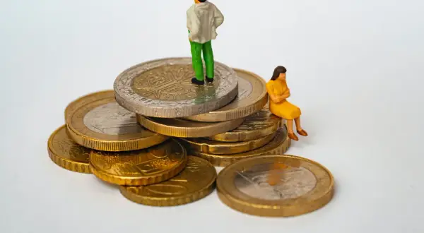 Figurki ludzi na stosie monet. Jedna osoba stoi na szczycie, druga siedzi obok. Symbolizuje to opłatę skarbową i jej wpływ na finanse.