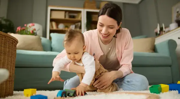 Mama bawi się z dzieckiem na dywanie, budując tory dla pociągu. To czas na zabawę i rozwijanie umiejętności, czyli aktywnie w pracy nad rozwojem malucha.