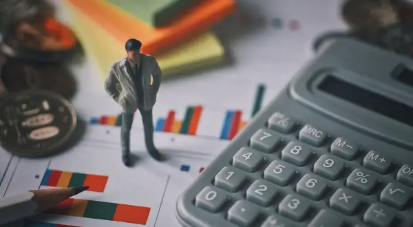Figurka mężczyzny, kalkulator, monety i wykresy. Czy to syndyk, kto to? Analiza finansowa.