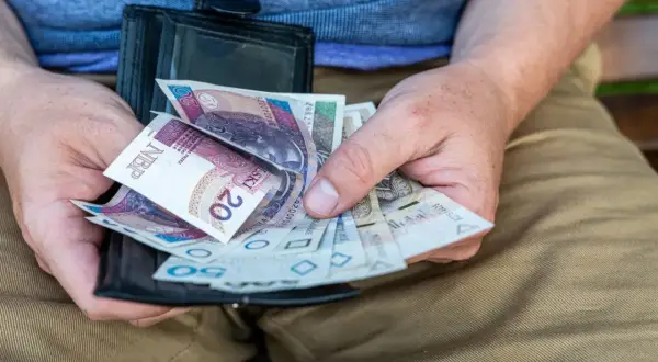 Dłonie trzymają portfel z polskimi banknotami. To może być świadczenie przedemerytalne, które zapewnia stabilność finansową.