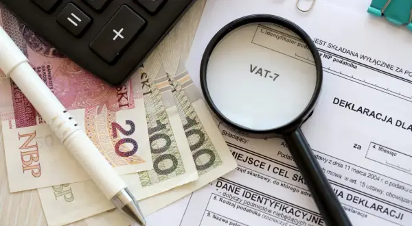 Pióro, banknoty, kalkulator i lupa nad deklaracją VAT-7. Przygotowanie do rozliczenia podatku.