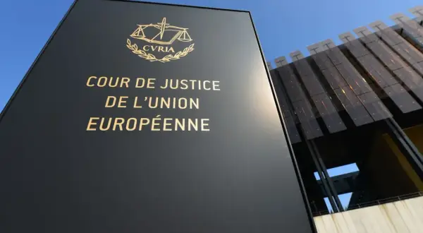 Czarny szyld z napisem "COUR DE JUSTICE DE L'UNION EUROPÉENNE" i symbolem wagi. W tle nowoczesny budynek.