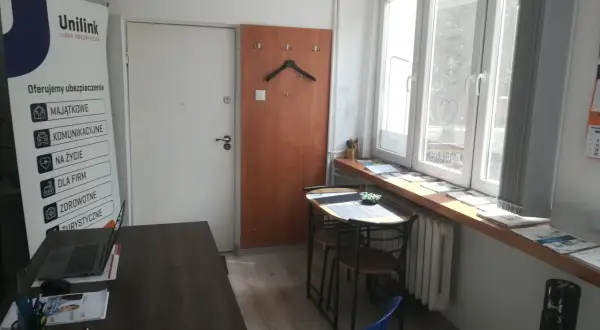 Biuro Unilink z banerem informacyjnym, biurkiem z laptopem i oknem.