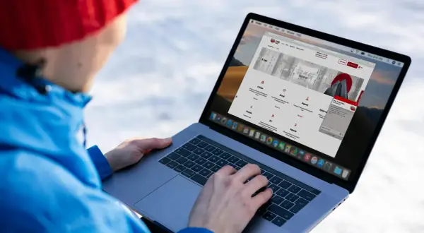 Osoba w czerwonej czapce i niebieskiej kurtce korzysta z laptopa, na ekranie którego widoczna jest strona internetowa KRD.