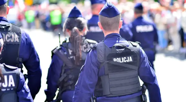 Policjanci w mundurach, tworzący zgraną kartę rodziny mundurowej, patrolują ulicę. Na kamizelkach taktycznych widnieje napis "POLICJA".